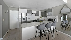 A modern kitchen with a central island, bar stools, and a large mirror. - Modern 3-bed Apt Designer Touch Mountain Views (Cape Town)