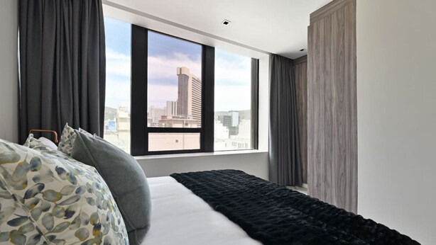 A modern hotel room with a large bed, dark curtains, and a city view through a large window. - 15th-floor 2-bed Panoramic City Views Modern Living (Cape Town)