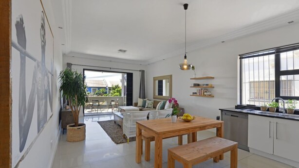A modern kitchen with white cabinets, a wooden dining table, and a large window. - Modern 2-bed Green Point Haven Stylish Central (Cape Town)