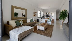 A spacious living room with a large sofa, a coffee table, and a dining area. There is a kitchen in the background with modern appliances. - Modern 2-bed Green Point Haven Stylish Central (Cape Town)