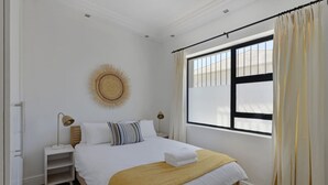 A neatly arranged bedroom with a bed, bedside tables, a wall decoration, and a window with curtains. - Modern 2-bed Green Point Haven Stylish Central (Cape Town)