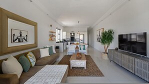 A modern living room with a sofa, coffee table, and TV. There is a kitchen in the background with a dining area. - Modern 2-bed Green Point Haven Stylish Central (Cape Town)
