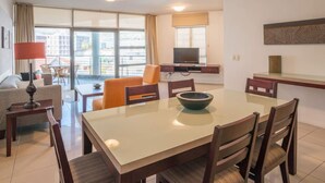 A hotel room with a dining area, a sofa, a TV, and a balcony with a view of buildings. - 6th Floor - 3bed City Center Spacious Secure (Cape Town)