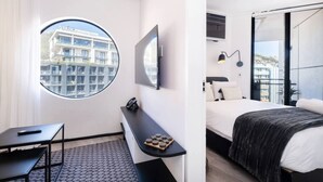 A modern hotel room with a large window, a bed, a desk, and a small seating area. - The Flamingo One Bed Sea Point Promenade (Cape Town)