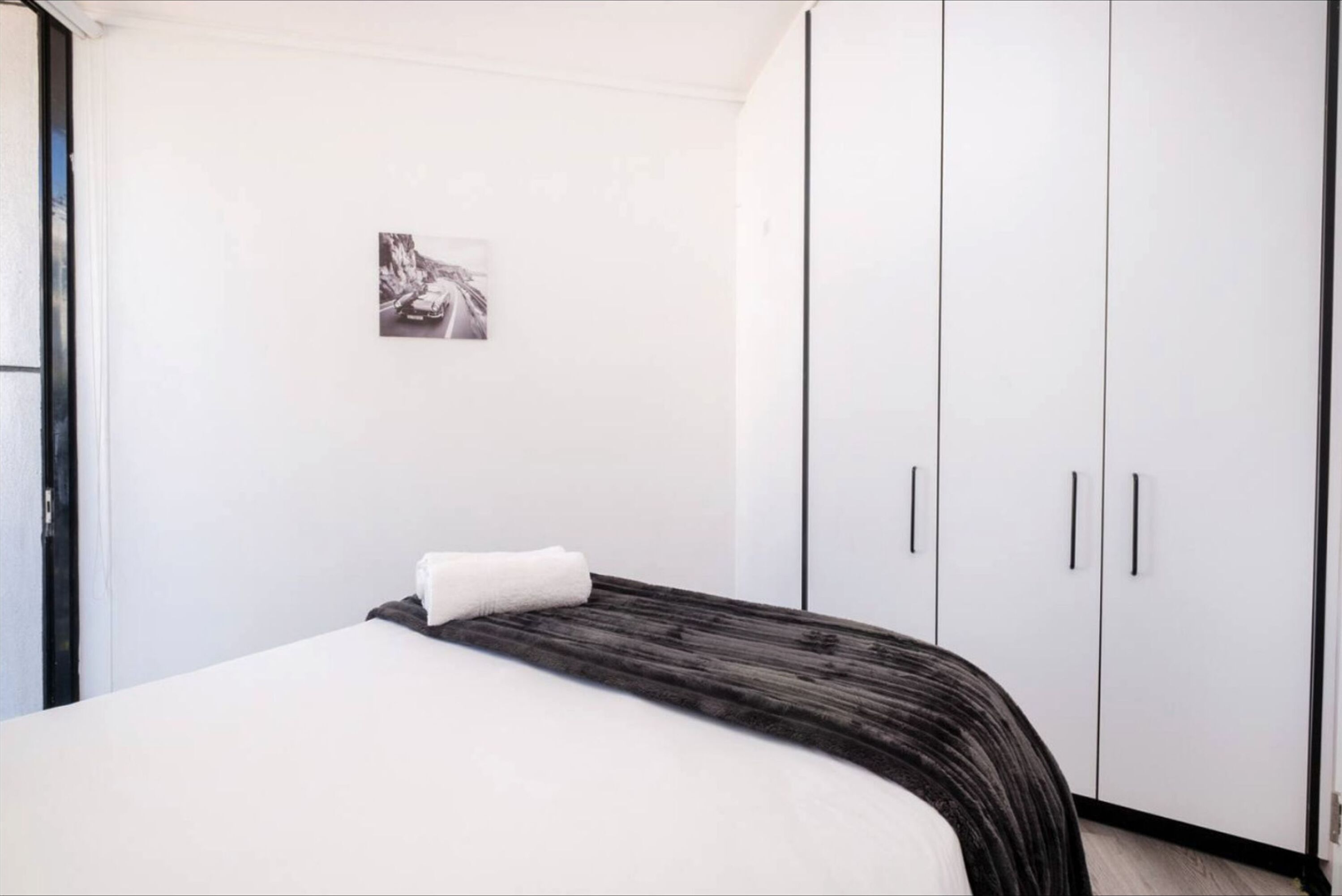 Une chambre à coucher avec un lit, un mur blanc, une photographie en noir et blanc et des armoires blanches.