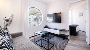 A modern hotel room with a large window, a flat-screen TV, a small table, and a bed. - The Flamingo One Bed Sea Point Promenade (Cape Town)