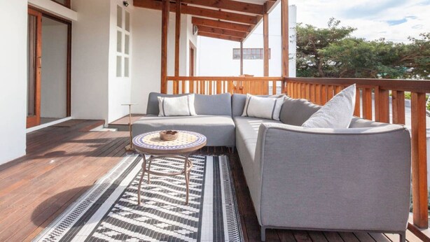 Un espace extérieur aménagé, abrité, avec un canapé et une petite table, un sol en bois et un tapis à motifs.