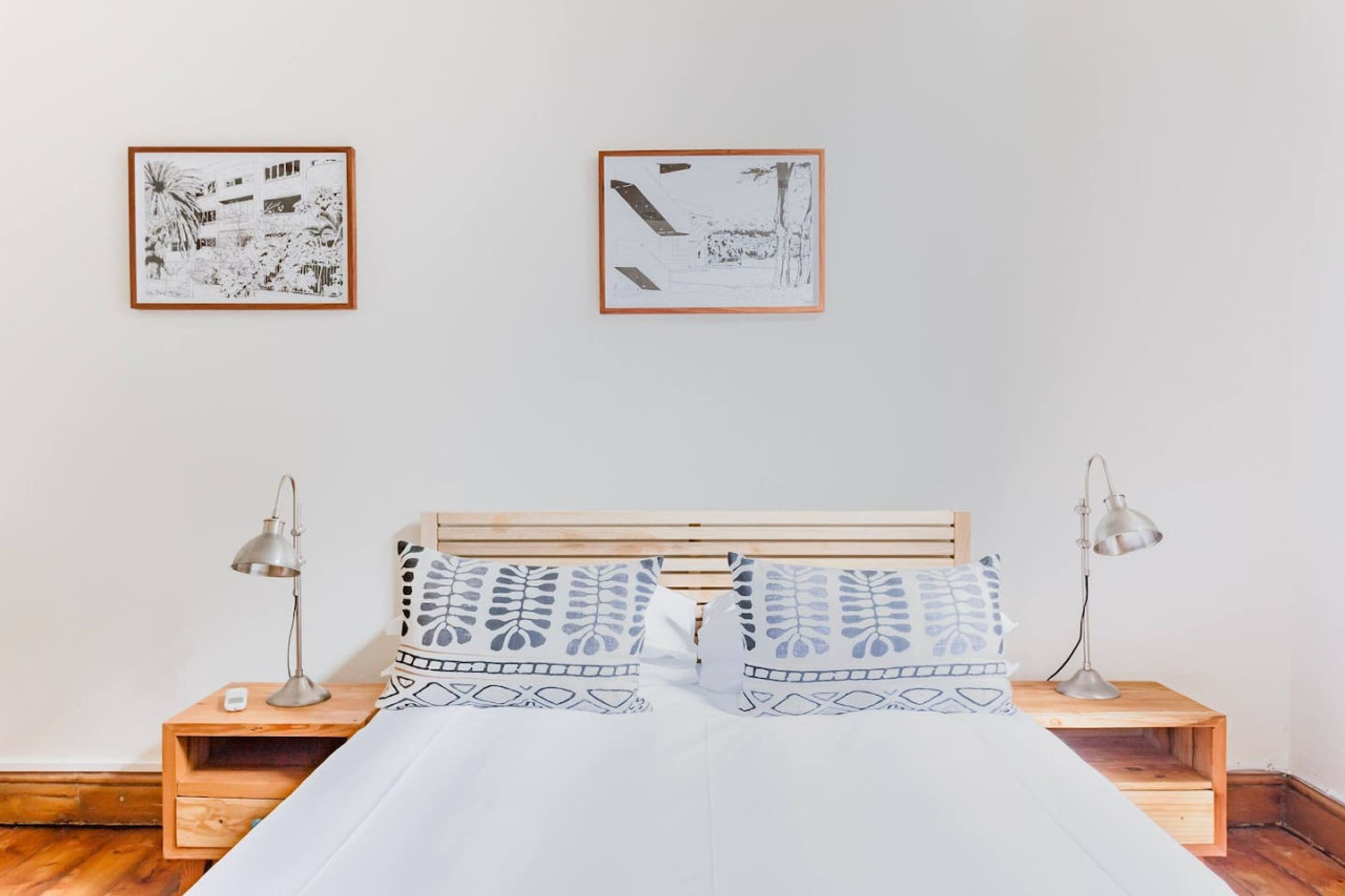 A bedroom with a wooden bed, two nightstands, two lamps, and two framed pictures on the wall.