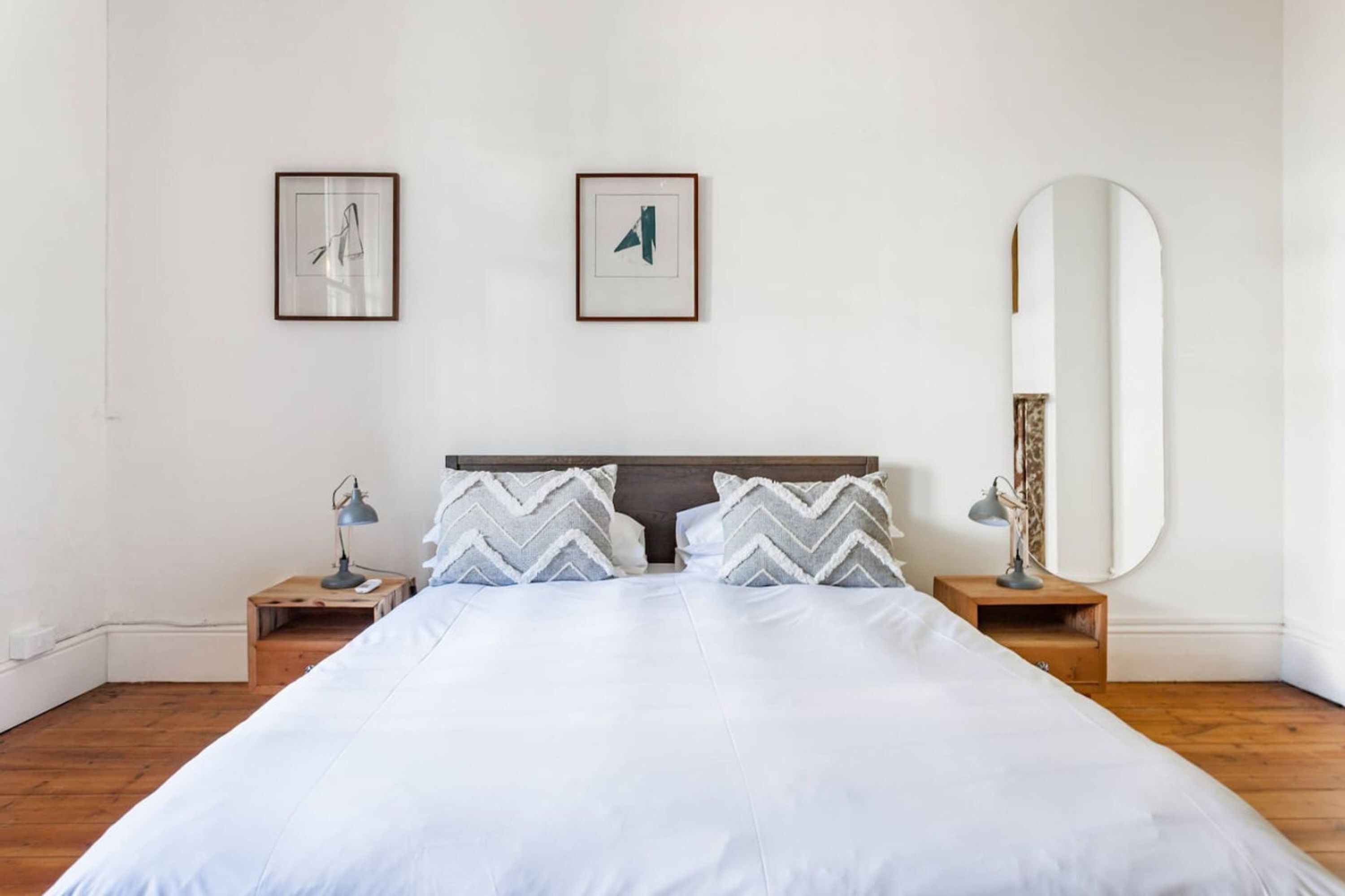 A neatly made bed with two pillows, a large mirror, and two framed pictures on the wall.