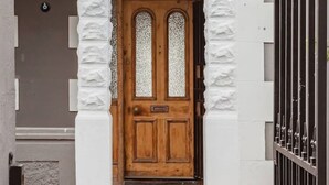 Une porte en bois avec un panneau de verre, flanquée de colonnes blanches, qui donne sur une entrée pavée de briques.