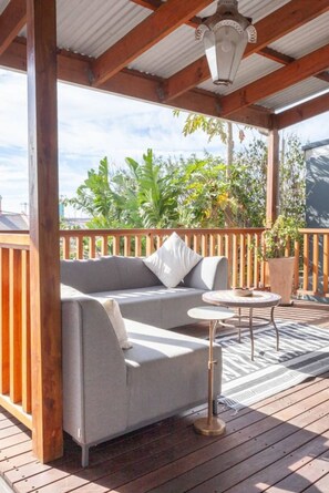 A covered outdoor seating area with a sofa and a small table, surrounded by a wooden deck and a railing. - Spacious 3-bed Sunlit Comfort Power Backup (Cape Town)