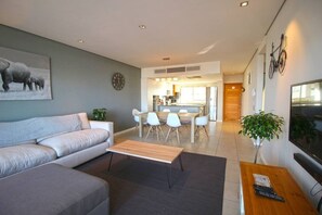 A modern living room with a sofa, a coffee table, and a dining area with chairs and a table. - Upmarket 2bed City Retreat Close to V A Waterfront (Cape Town)