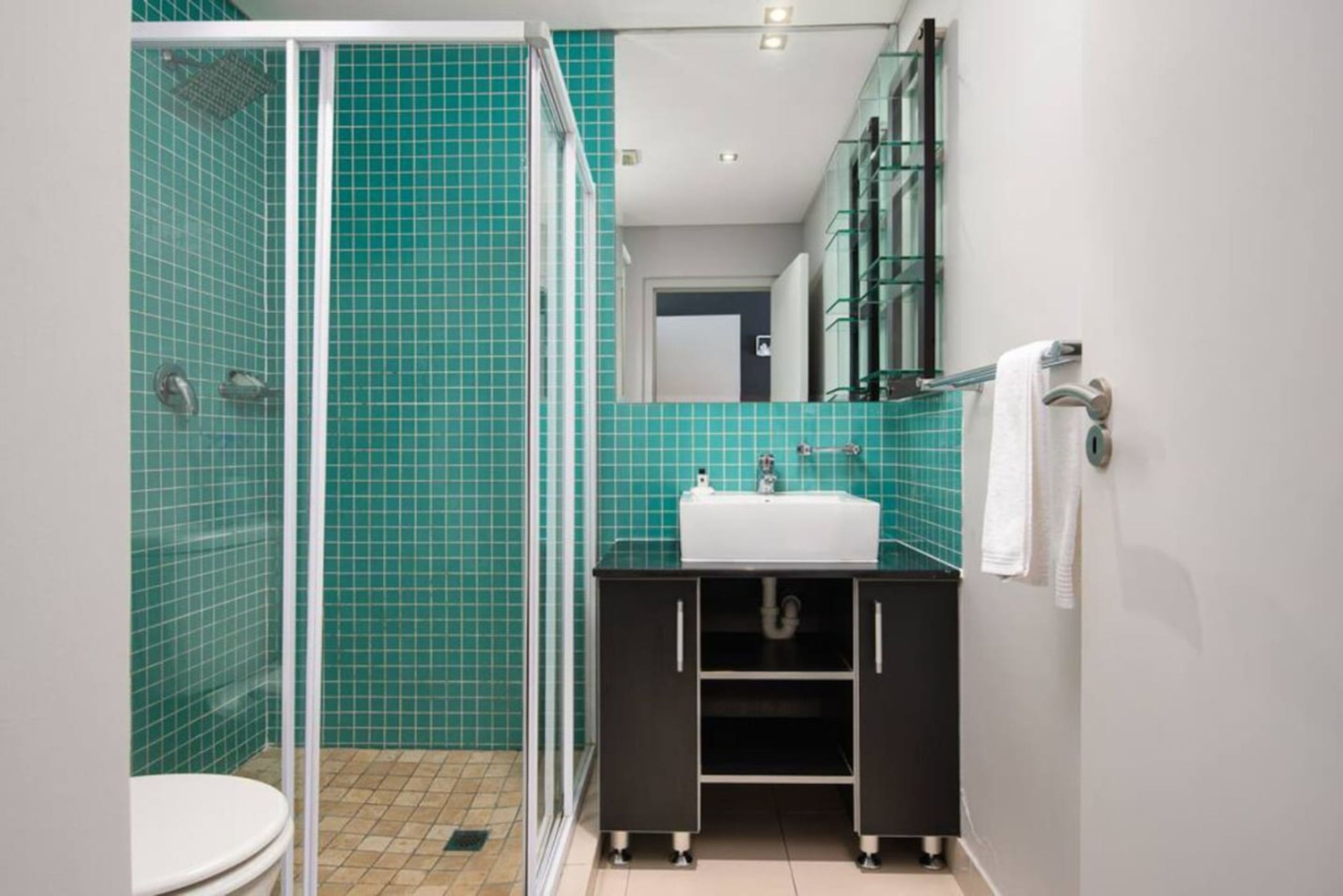 A bathroom with a glass shower enclosure, a white sink, and a dark cabinet.