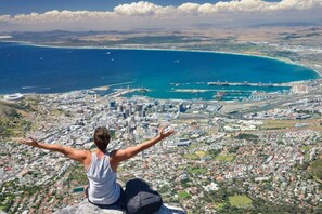 Une personne se tient au bord d’une falaise surplombant une ville côtière, avec vue sur l’océan et un port de plaisance.