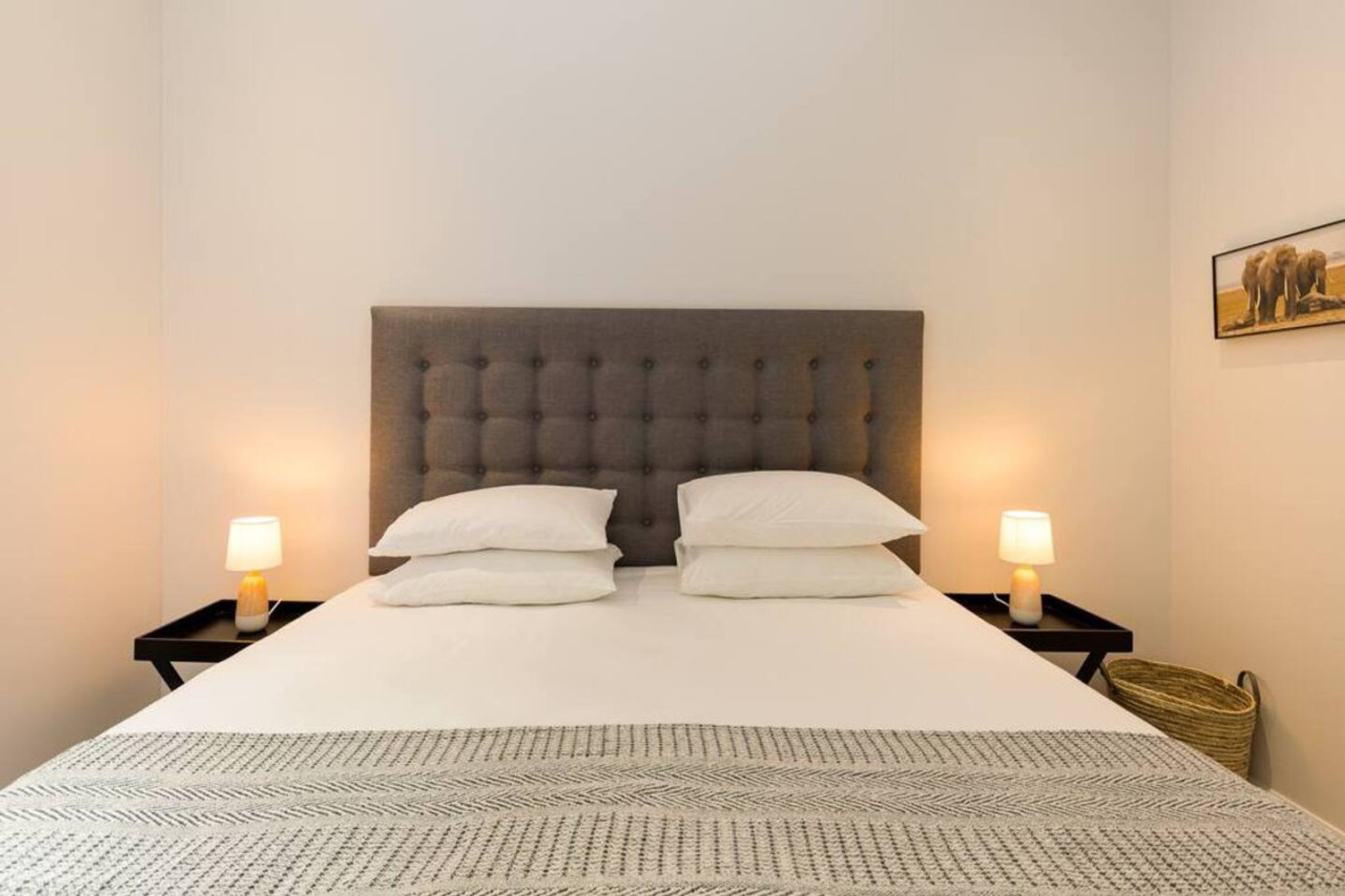 A neatly made bed with a tufted headboard, two bedside tables with lamps, and a patterned rug.