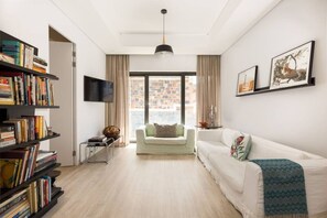 Una sala de estar moderna con un sofá blanco, una estantería, un televisor de pantalla plana y un amplio ventanal con vistas a la ciudad.