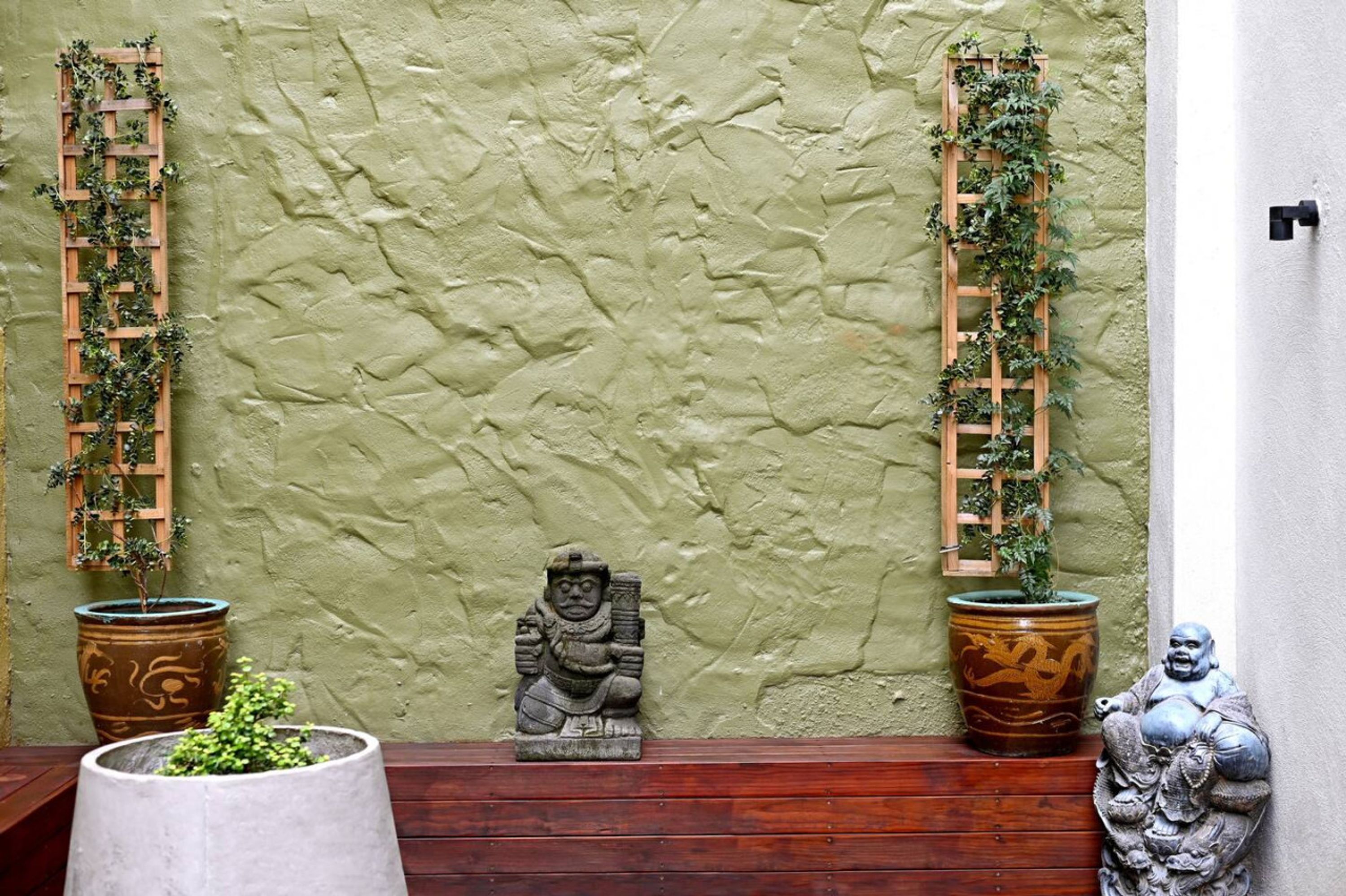 A stone statue with a traditional design, a wooden ladder with greenery, and a large decorative pot.