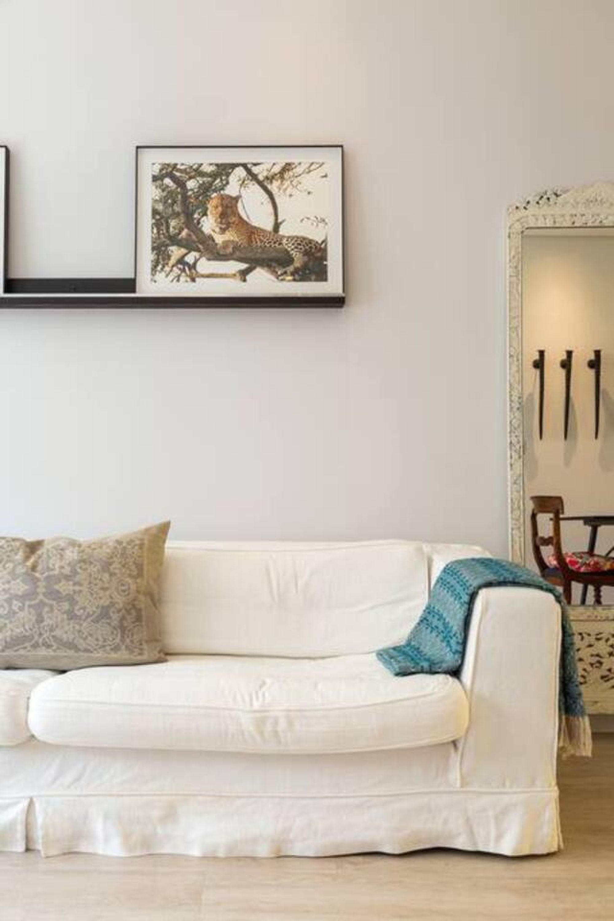 Un canapé blanc surmonté d’un plaid bleu, un tableau encadré représentant un léopard et un miroir doté d’un cadre décoratif.