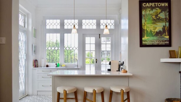 A bright kitchen with a large island, three stools, and a window with a view of greenery. - Spacious 3 Bedroom Home Green Point (Cape Town)