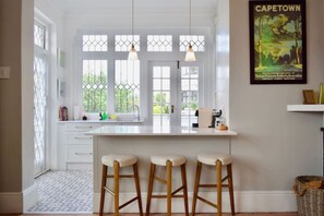 A bright kitchen with a large island, three stools, and a window with a view of greenery. - Spacious 3 Bedroom Home Green Point (Cape Town)