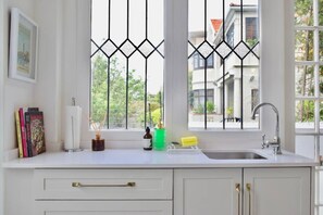 A kitchen with a window, white cabinets, a sink, and a window with a decorative metal grille. - Spacious 3 Bedroom Home Green Point (Cape Town)