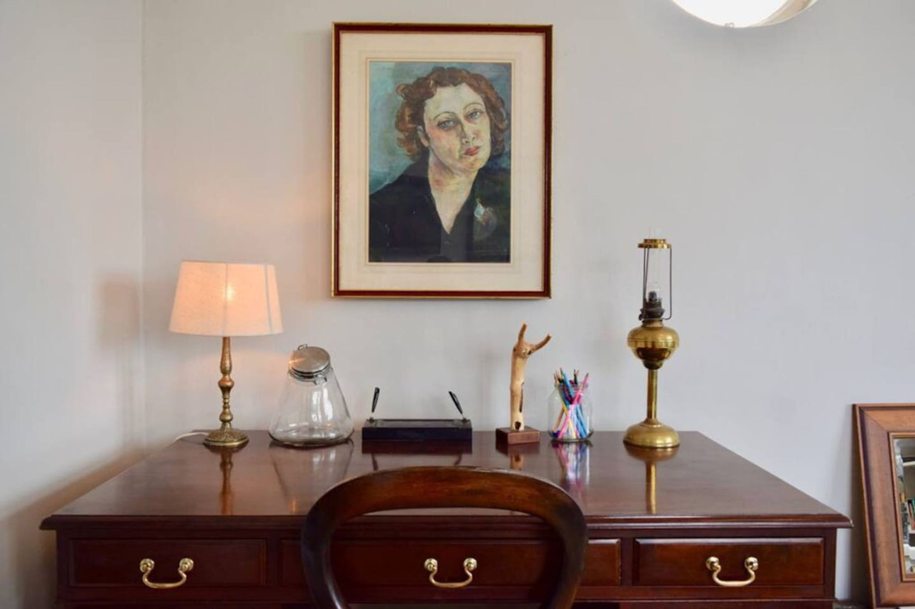 A wooden desk with a framed painting, two brass lamps, and various desk accessories.
