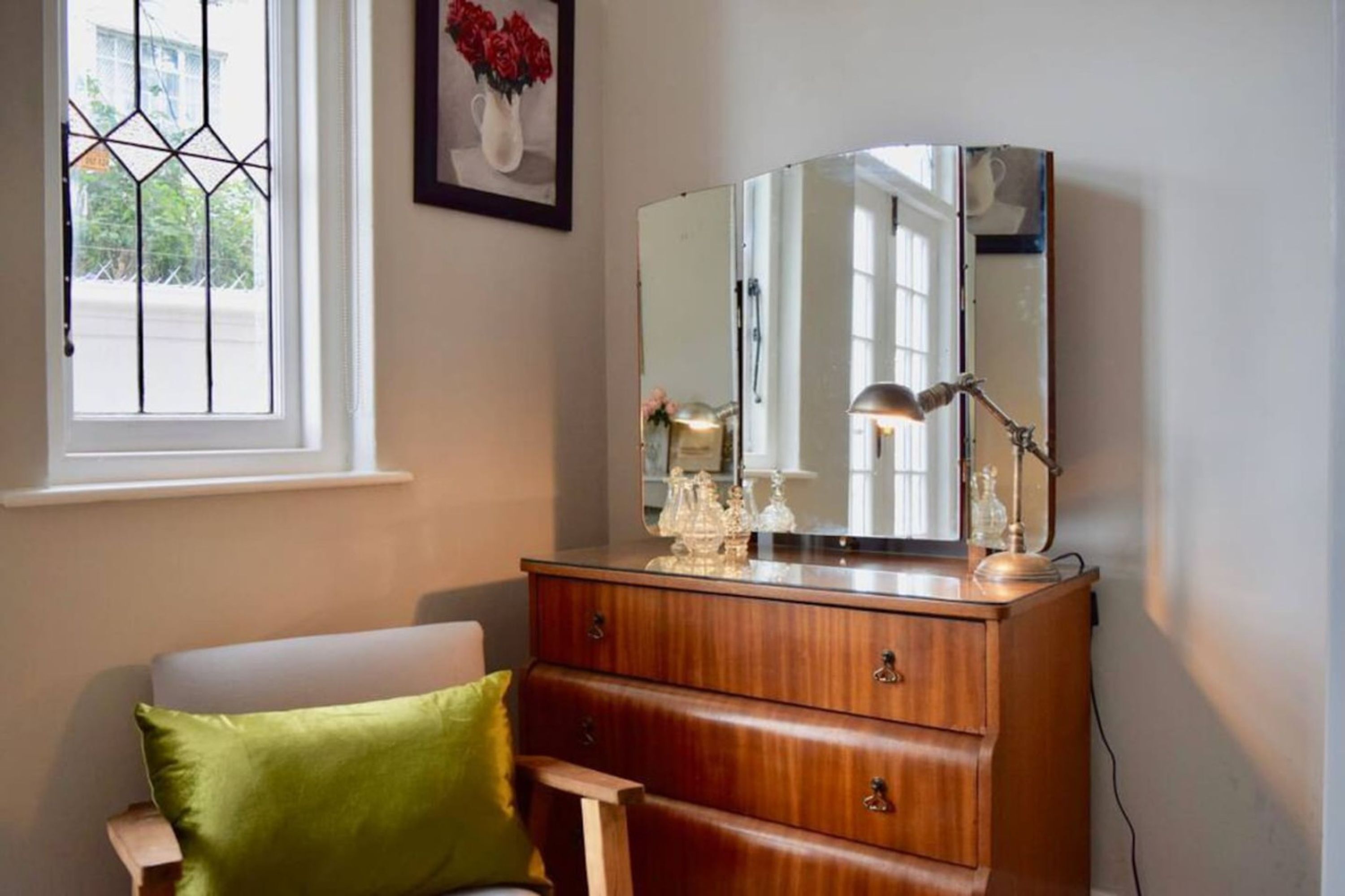 A room with a wooden dresser, a mirror, and a green pillow on a chair.