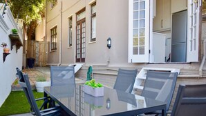 An outdoor patio with a glass table and chairs, surrounded by a wooden deck and a small garden area. - Spacious 3 Bedroom Home Green Point (Cape Town)