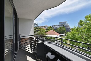 A balcony with a metal railing, a trash bin, and a view of surrounding buildings and trees. - Secure 2bed Green Point Retreat Rooftop Pool BBQ (Cape Town)