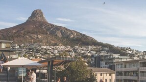 A rooftop pool area with a bar and lounge seating, overlooking a cityscape and a prominent mountain. - Modern Sea Point Apartment Rooftop Pool (Cape Town)