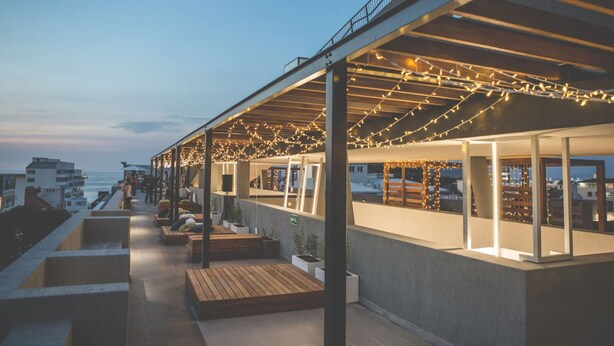 A rooftop terrace with string lights, seating areas, and a view of the ocean. - Modern Sea Point Apartment Rooftop Pool (Cape Town)