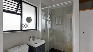 A modern bathroom with a glass-enclosed shower, a white sink, and a toilet. - Charming 2-bed Central Green Point Stadium (Cape Town)