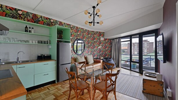A compact kitchen with a dining area, a large window, and a view of buildings. - Charming 2-bed Central Green Point Stadium (Cape Town)