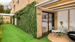 A courtyard with artificial grass, a green wall, a dining area with chairs and a table, and a barbecue grill. - Cosy One Bed Table Mountain (Cape Town)