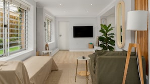 A modern living room with a large TV, a sofa, a small table, and a large plant. - Cosy One Bed Table Mountain (Cape Town)