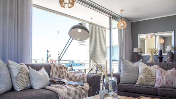 Een moderne woonkamer met een grijze bank, een bijzettafeltje met een spel en een groot raam met gordijnen.
