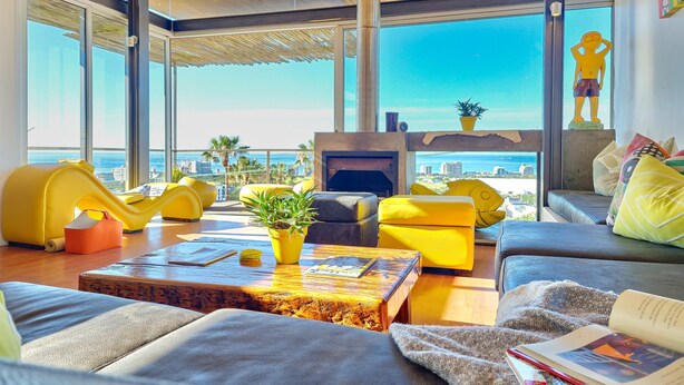 A modern living room with yellow sofas, a wooden coffee table, and a fireplace. - Ocean Views Open Plan Pool 3 Bed (Cape Town)