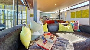 A modern living room with a sofa, cushions, and a book. - Ocean Views Open Plan Pool 3 Bed (Cape Town)