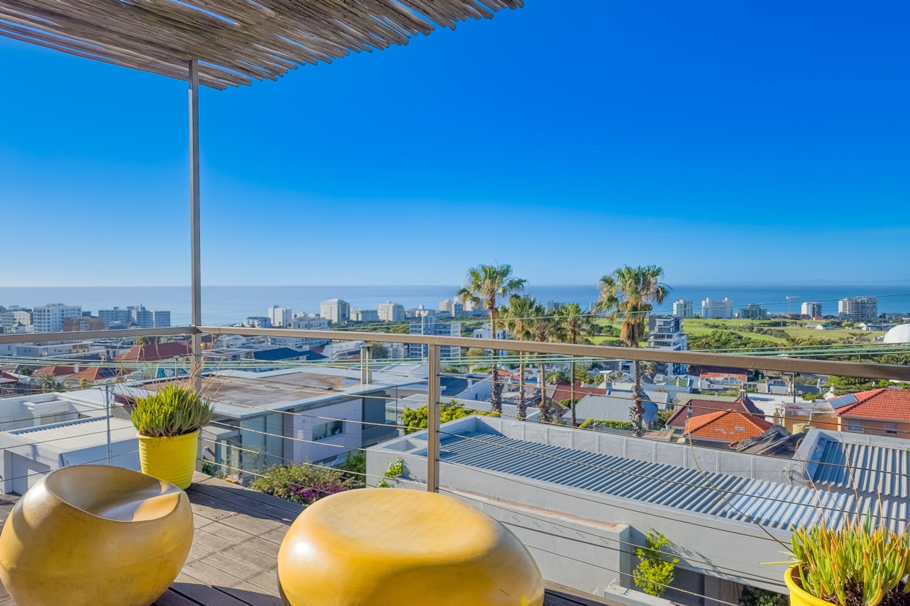 A rooftop terrace with a clear view of the city skyline, palm trees, and a distant body of water.