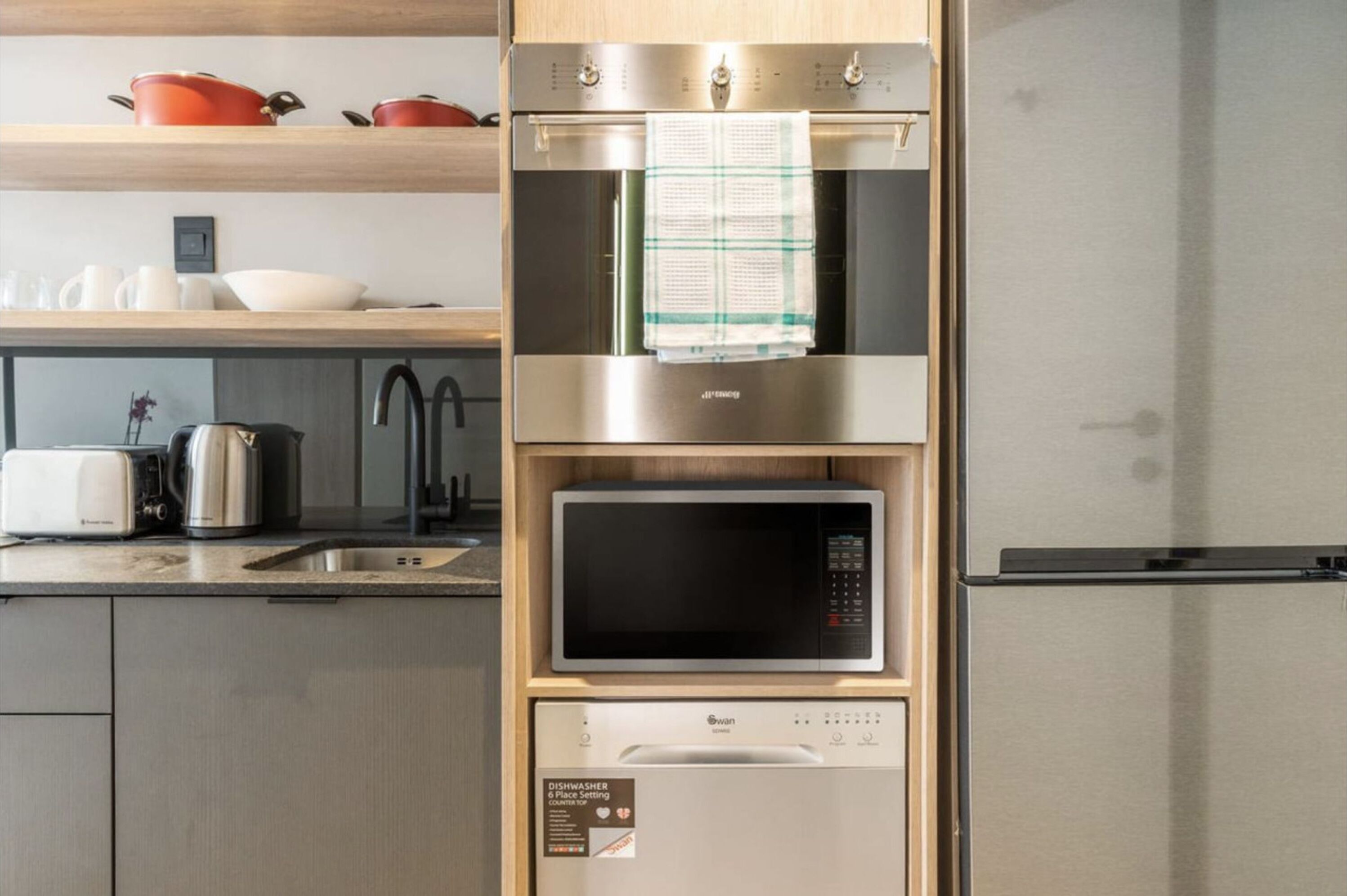 A compact kitchen with a built-in oven, microwave, and dishwasher, and a stainless steel refrigerator.