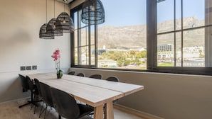 A conference room with a long table, black chairs, and a large window with a view of buildings and mountains. - Modern Apt Co-working East City (Cape Town)