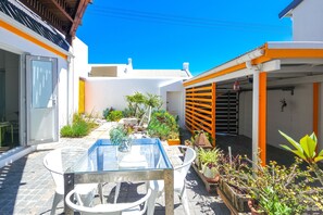 A courtyard with a glass table and chairs, surrounded by potted plants and a small garden. - Green Point Peaceful Retreat Off-grid (Cape Town)