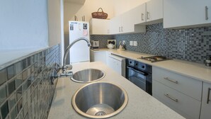 A modern kitchen with two stainless steel sinks, a microwave, a kettle, and a basket on the countertop. - Green Point Peaceful Retreat Off-grid (Cape Town)