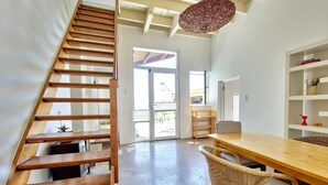 A modern interior with a wooden staircase, a dining area with wicker chairs, and a large window with a view of the outdoors. - Green Point Peaceful Retreat Off-grid (Cape Town)