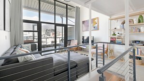 Ein modernes Wohnzimmer mit großem Fenster, grauem Sofa und einer Treppe, die in einen oberen Bereich führt.