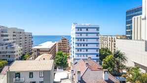 Un paysage urbain côtier avec des bâtiments modernes, un ciel bleu dégagé et une vue sur la mer.
