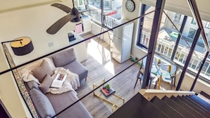 Un appartement moderne avec un escalier menant à un balcon, un canapé gris, une petite table avec une plante et une vue sur la ville.