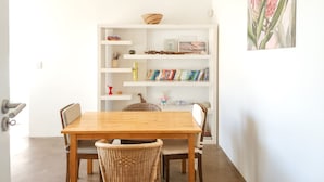 A dining area with a wooden table and wicker chairs, a white bookshelf with various items, and a painting on the wall. - Peaceful Retreat Green Point Off-grid (Cape Town)