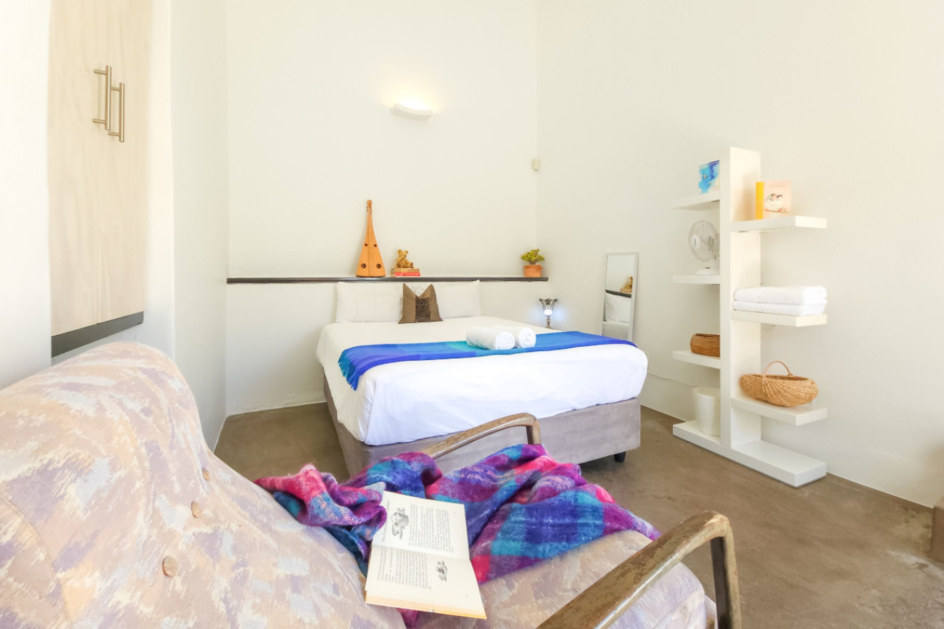 A bedroom with a bed, a bedside table, a chair, a bookshelf, and a wardrobe.