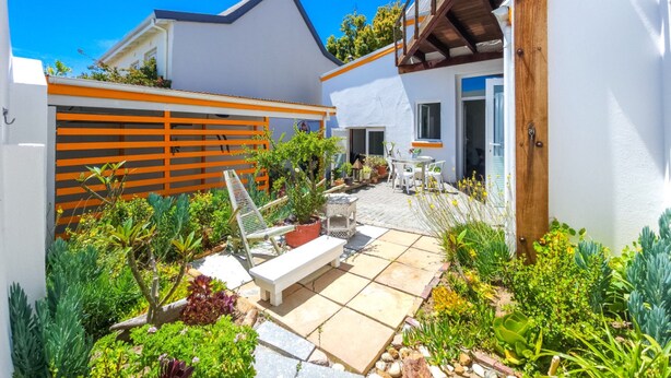 A modern outdoor patio area with a white building, wooden deck, and various plants. - Peaceful Retreat Green Point Off-grid (Cape Town)